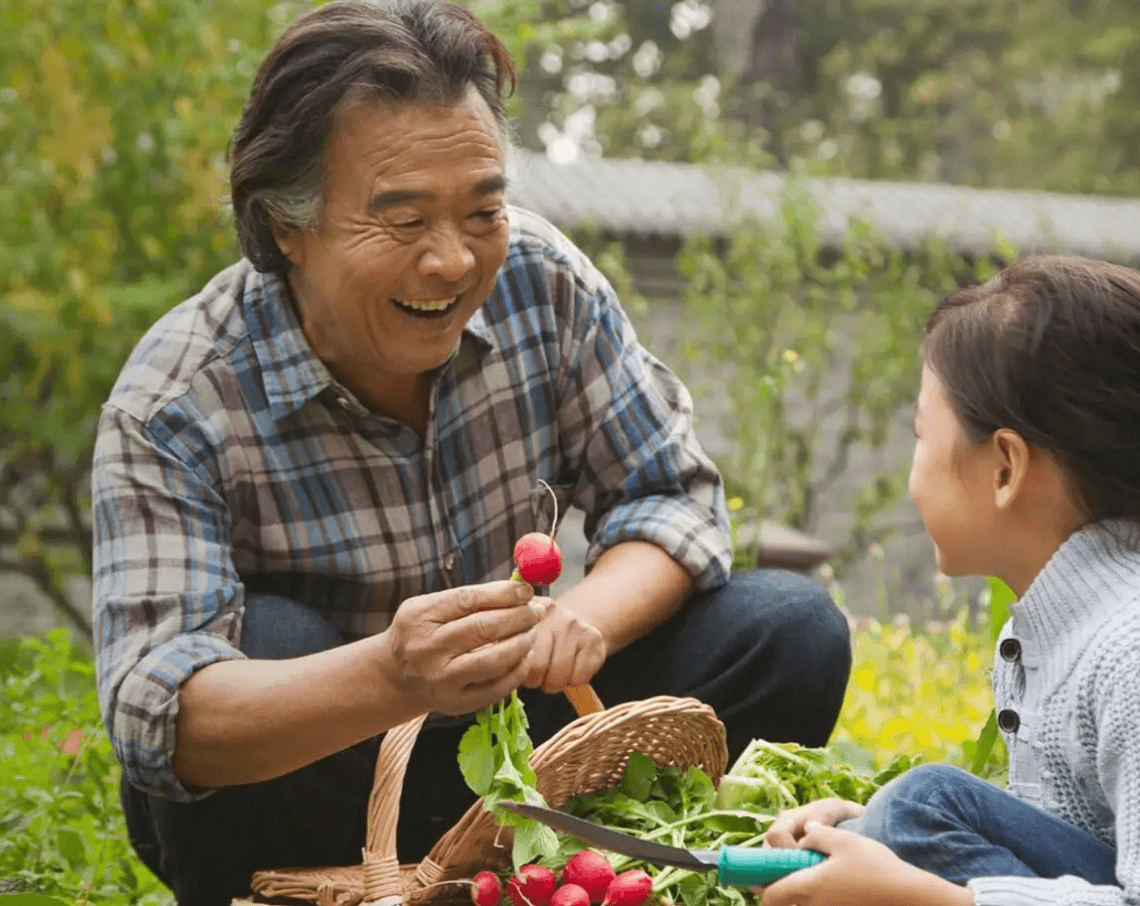 Photographie d'un senior en train de donner une tomate à une petite fille.